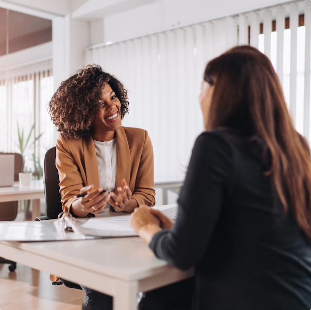 Two women sitting across a desk chatting