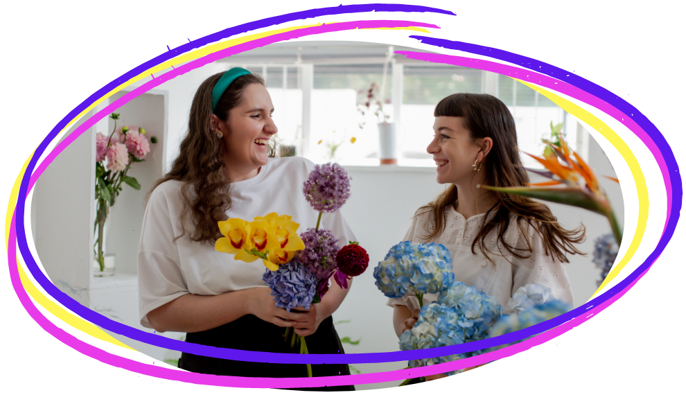 Two female work colleagues laughing in the corridor carrying flowers