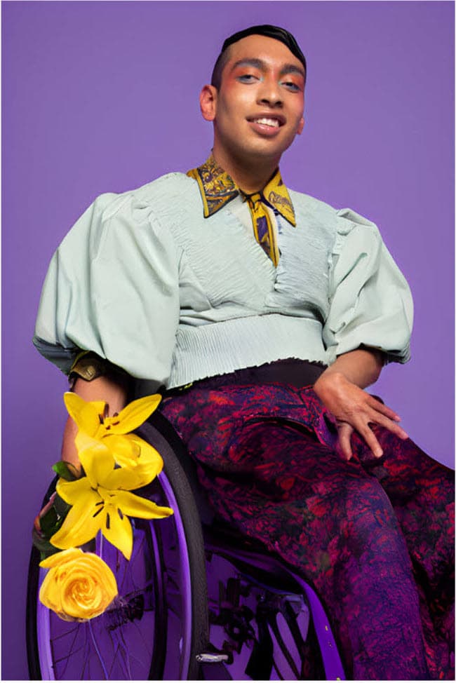 A young male with brown skin is in his wheelchair looking vey stylish with slick hair fabulous purple trousers holding bright yellow flowers